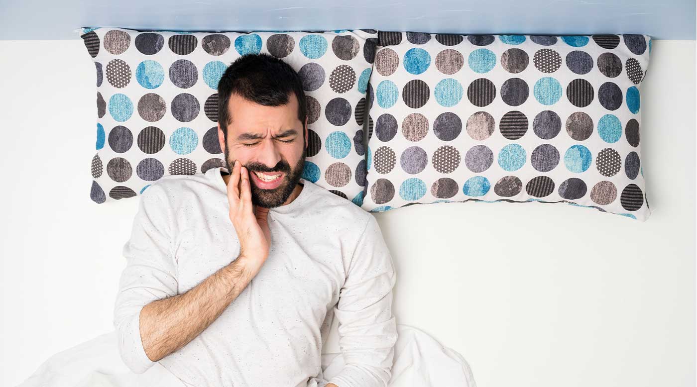 Mann liegt schlaflos im Bett, hält sich den Kiefer